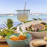 Food from formentera with a glass of mocktail and ocean in the background