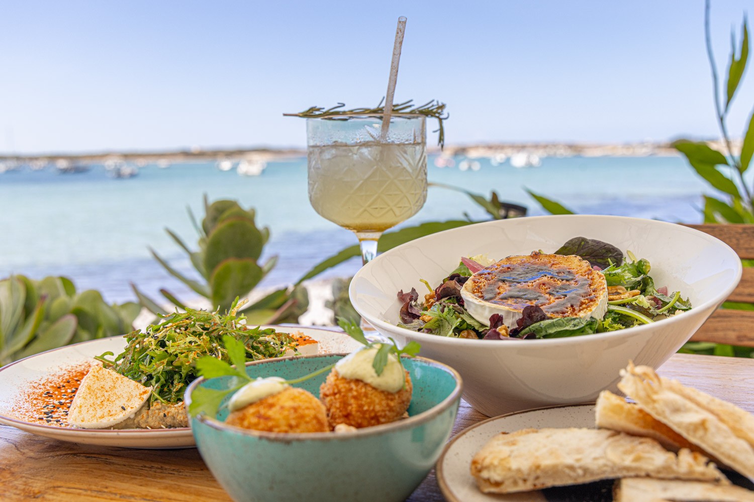 Food from formentera with a glass of mocktail and ocean in the background