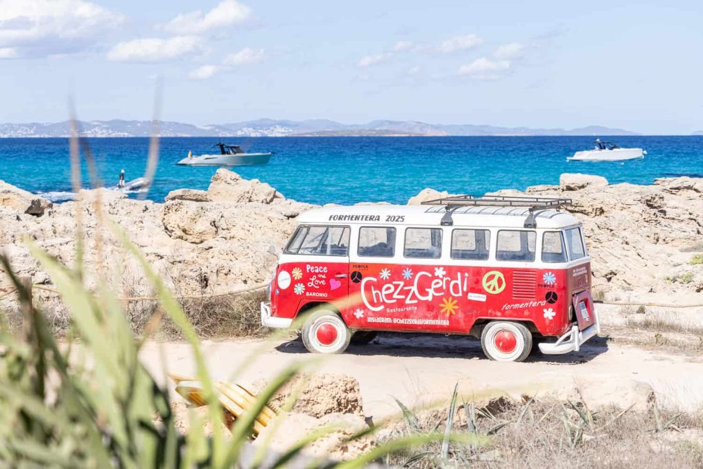A small vw buss with Chezz Gerdi logo by the sea